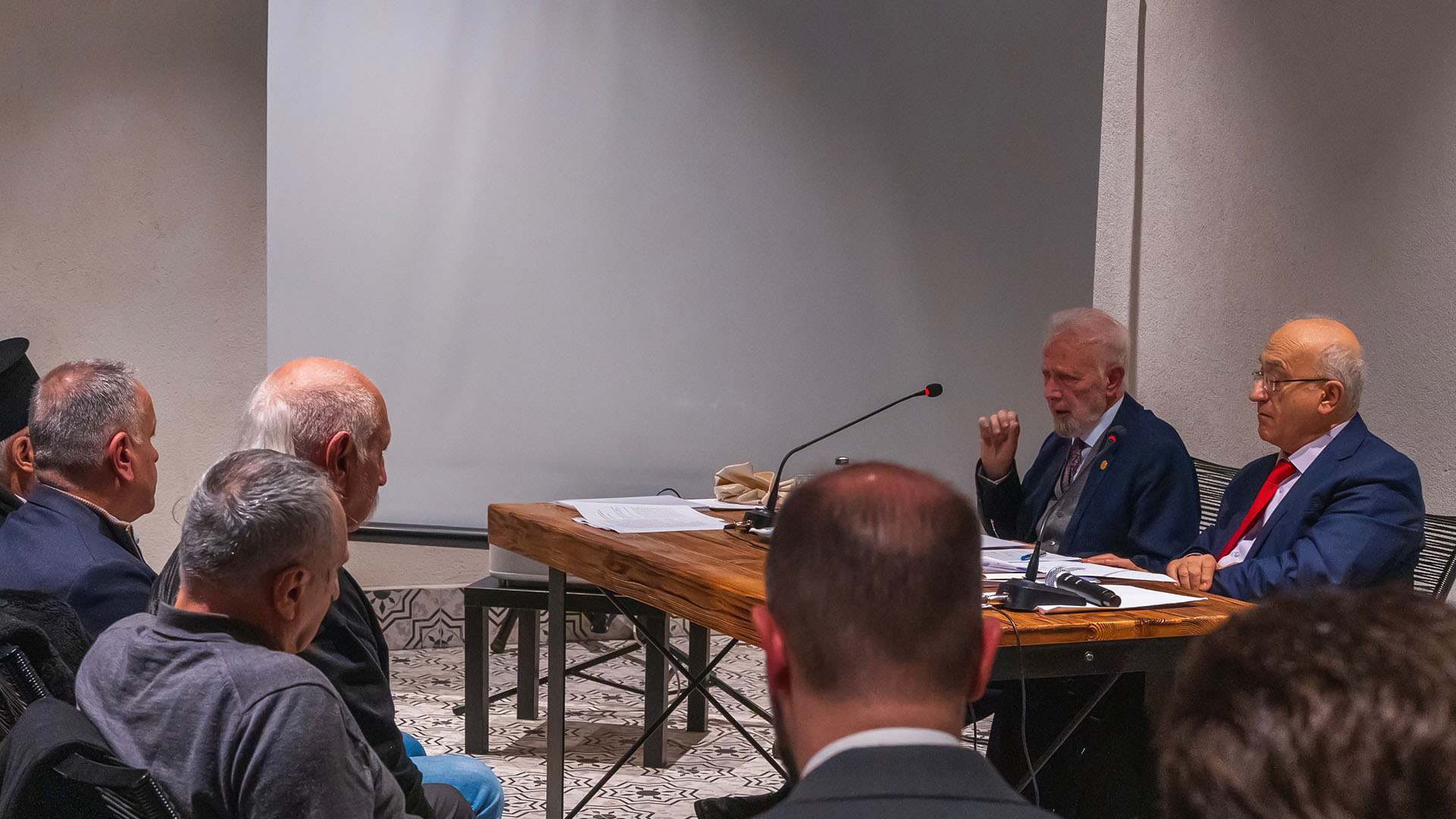 Professor Konstantinos Delikostantis speaking at a microphone during a theological panel lecture at the historic Panagia Paramythia church complex in Istanbul, with an audience seated in the foreground.